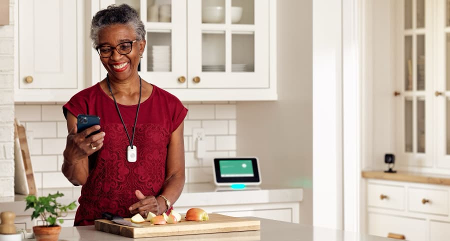 Woman in kitchen looking at her phone and wearing a Vivint medical alert pendant